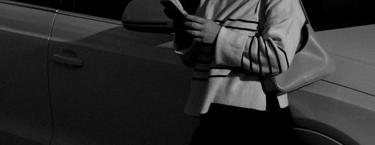 a woman standing next to a car looking at her cell phone