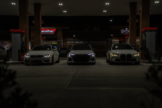 Three cars are parked at a gas station at night.