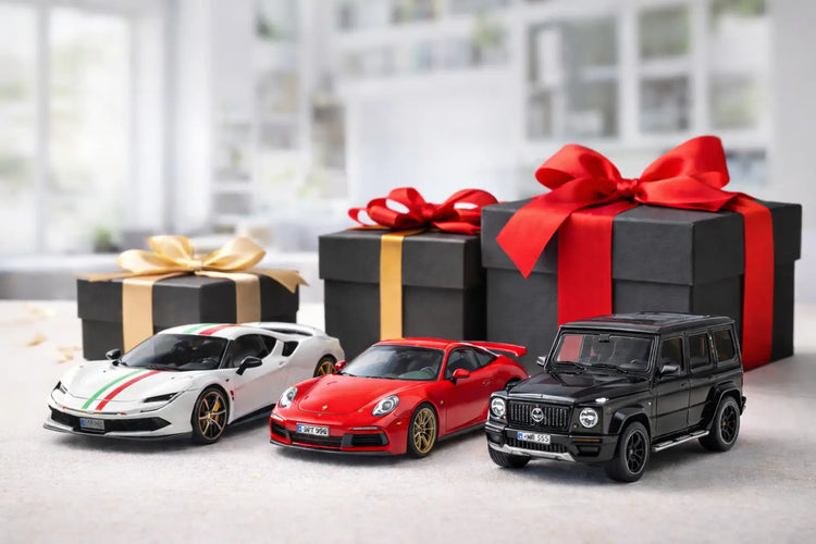 Trzy szczegółowe modele samochodów z odlewu ciśnieniowego — biały ferrari z zielono-czerwonymi paskami, jaskrawoczerwony porsche 911 i smukły czarny mercedes g-wagon — są wystawione przed zapakowanymi pudełkami prezentowymi.